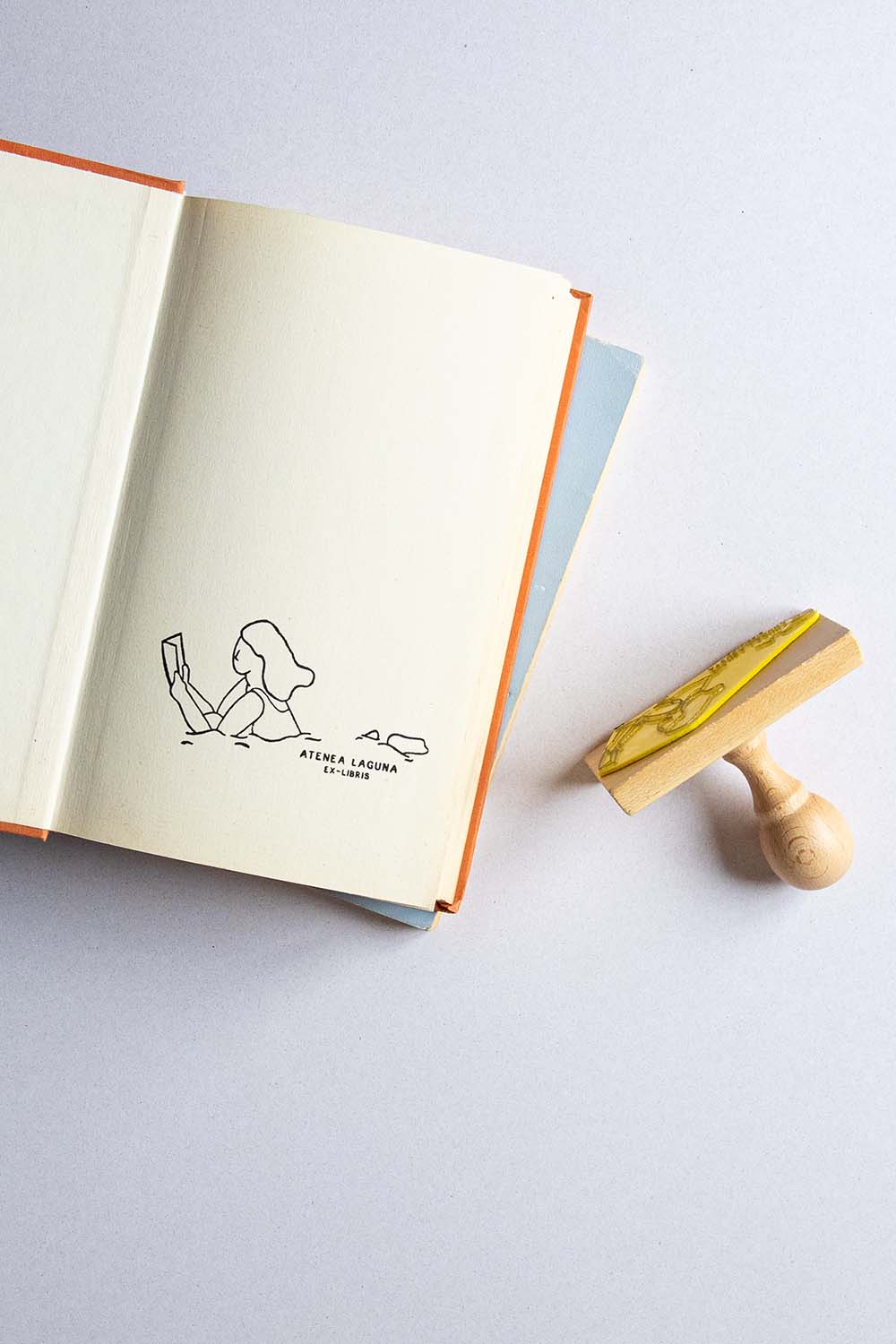 Portadilla de libro estampada con de una mujer nadando y leyendo un libro al mismo tiempo y sello