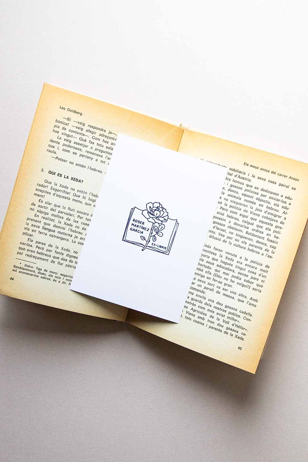 Portadilla de libro estampada con sello exlibris de un libro abierto con rosa encima