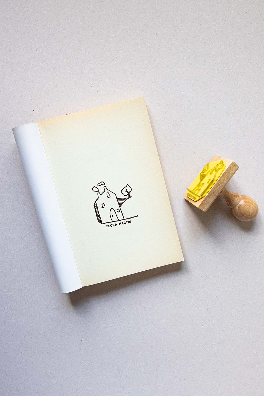 Portadilla de libro estampada con una casa en el campo con humo saliendo de la chimenea y un árbol al lado y sello