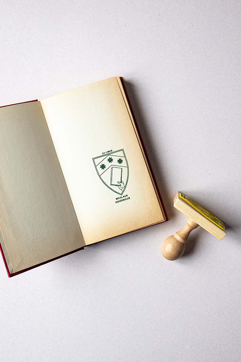 Portadilla de libro estampada con un escudo heráldico con una mano que sostiene un libro y tres estrellas