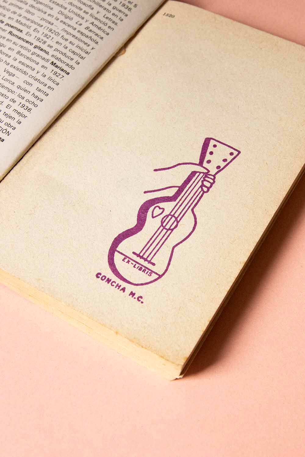 Portadilla de libro estampada con sello exlibris de una mano sosteniendo una guitarra
