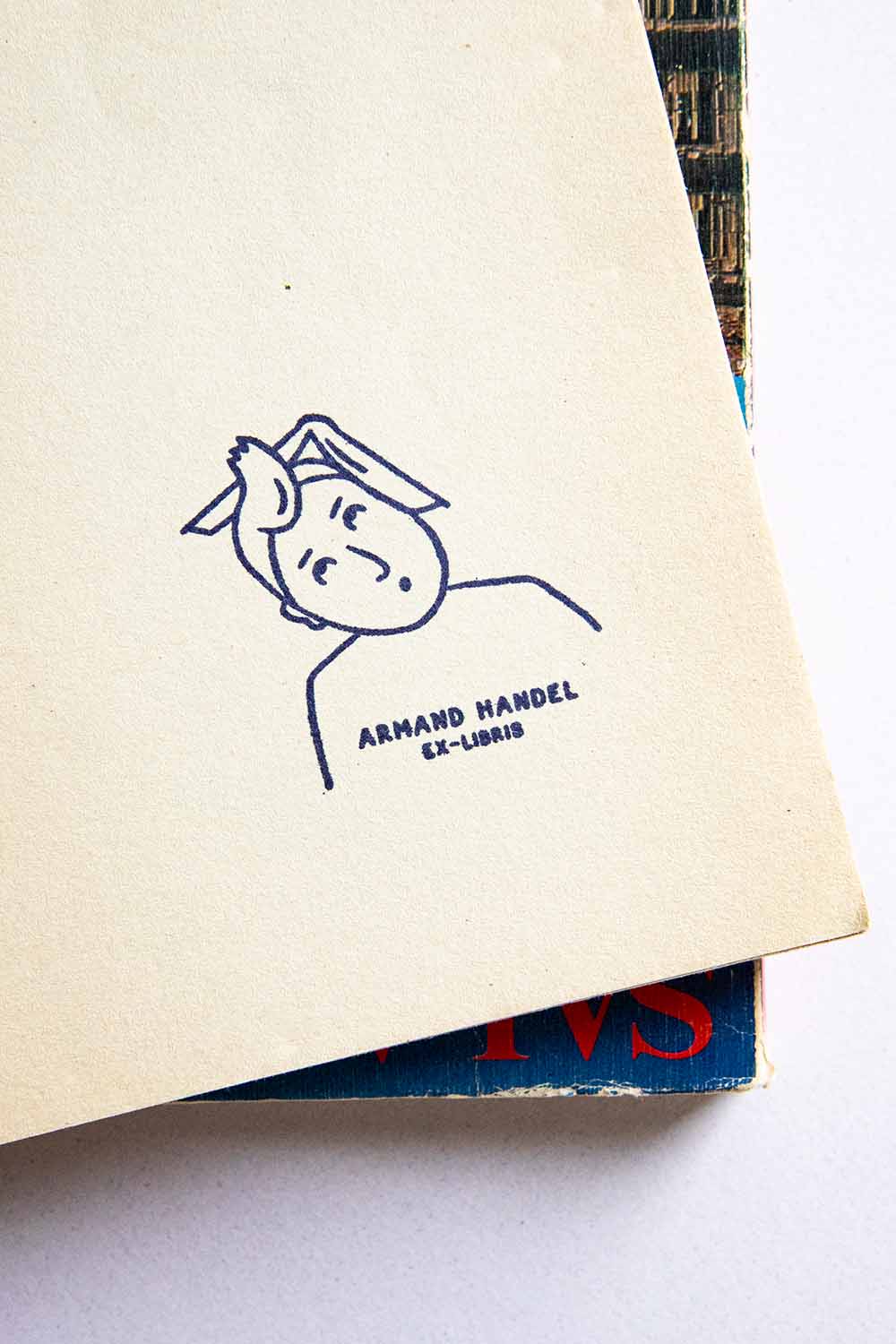 Portadilla de libro estampada con sello exlibris de un hombre sorprendido con un mechón de pelo hacia arriba y un libro sobre su cabeza