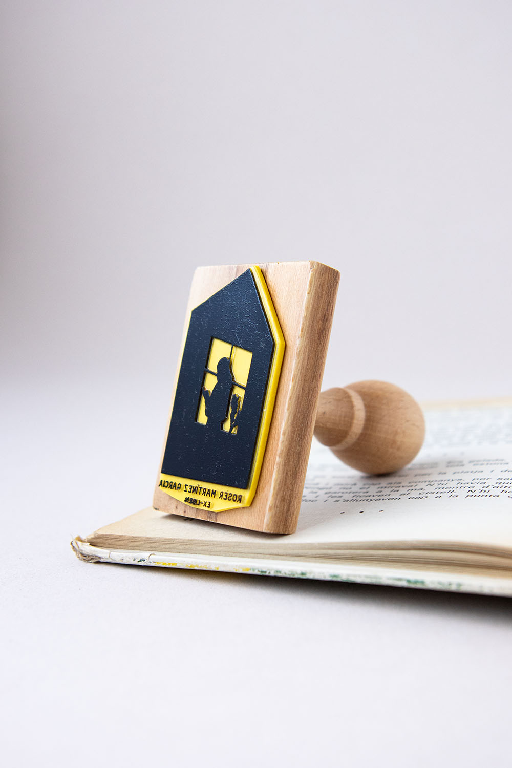 Sello exlibris grabado con una silueta de una persona leyendo un libro junto a una ventana