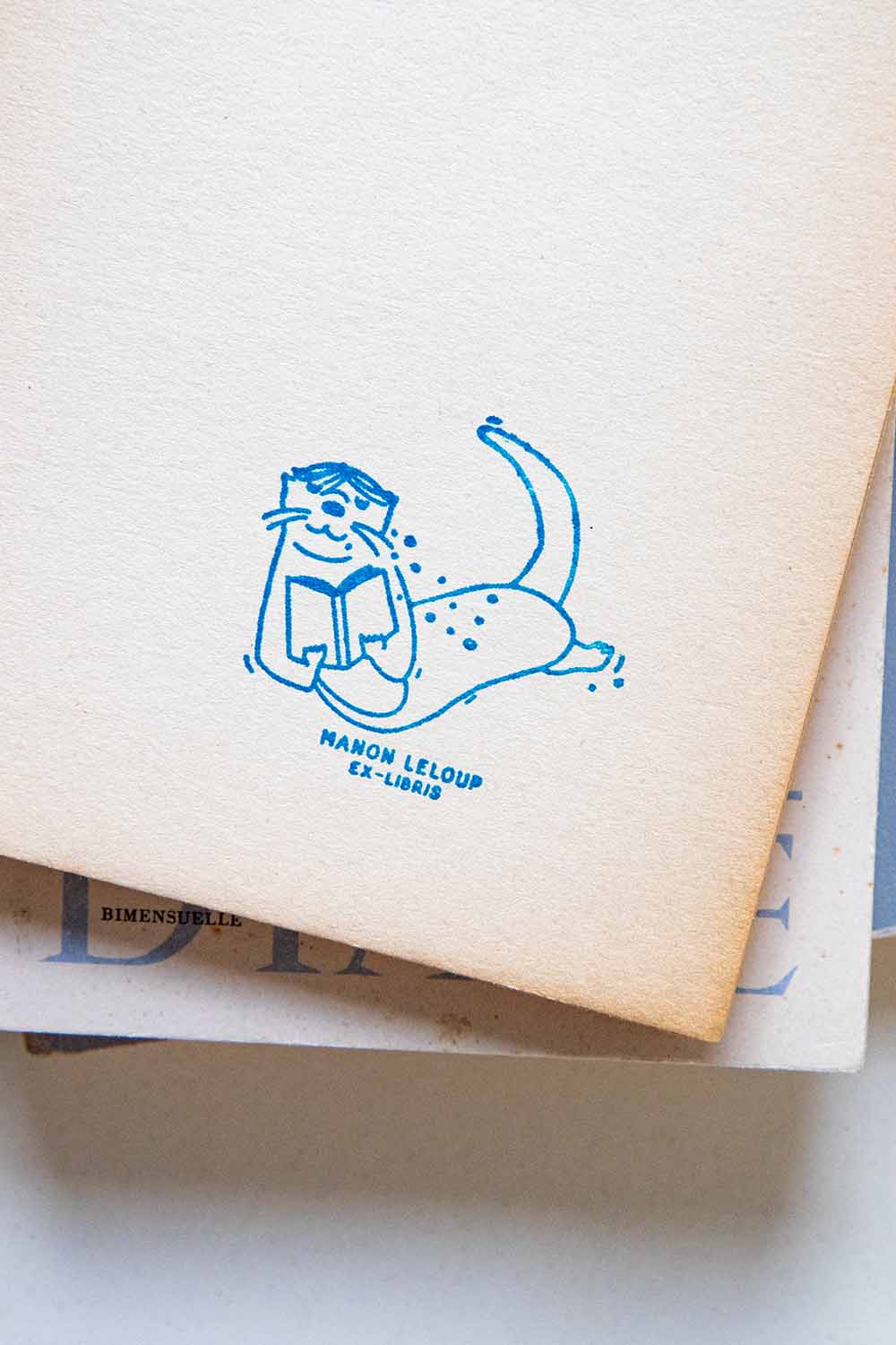 Portadilla de libro estampada con sello exlibris de una nutria leyendo bajo el agua